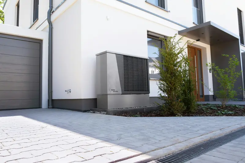 Outdoor heat pump unit installed in front of a modern white house