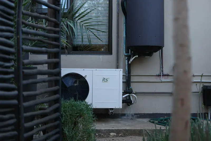 Outdoor air conditioning unit mounted beside a house next to a slatted fence